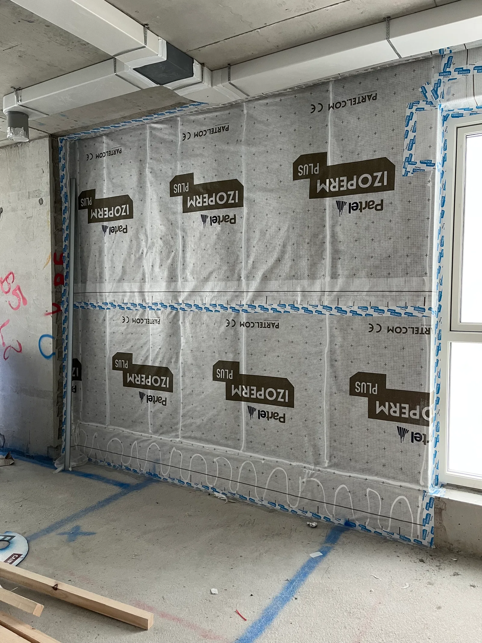 An airtightness membrane taped at every seam and around a window reveal in a concrete-frame building