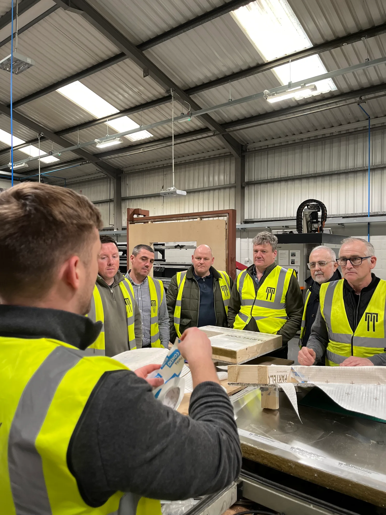 A crew of tradespeople in hi-vis being shown an airtightness tape detail on a timber and mineral wool mock-up